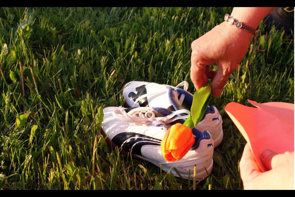 Attendees at Thursday night's tribute puts flowers into one of the 215 pairs of shoes laid out in tribute.