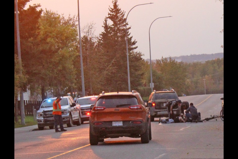 A vehicle stops on 103 Street as passers-by help to direct traffic and attend to a person lying on the roadway.
