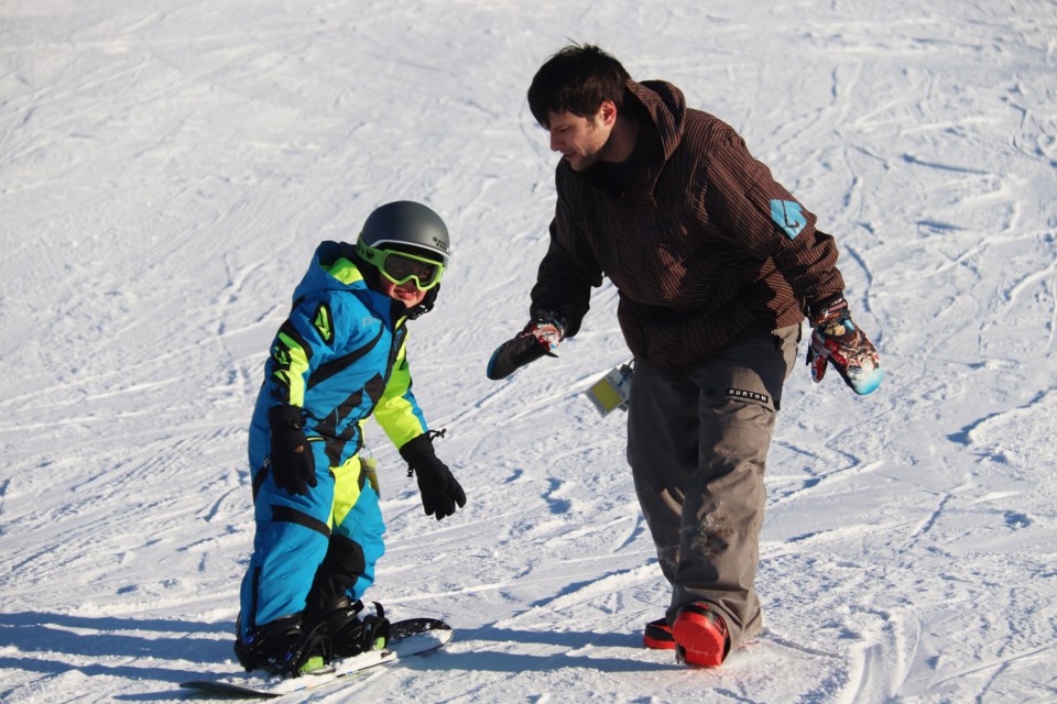 Four-year-old Felix Mailloux gets a few tips on how to keep his balance on a snowboard from his dad Chris. This was the young St. Paul resident's first time on the learner's hill at Kinosoo. Photo by Meagan MacEachern. 