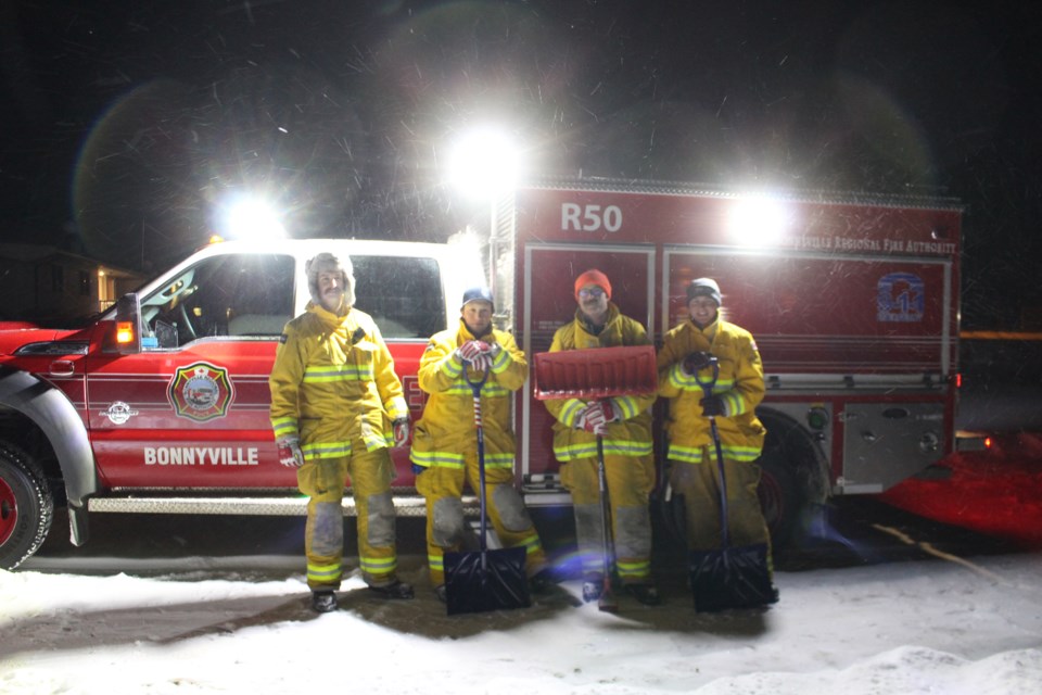 Under the lights of their fire truck, volunteers help to shovel the walkways of their neighbours.