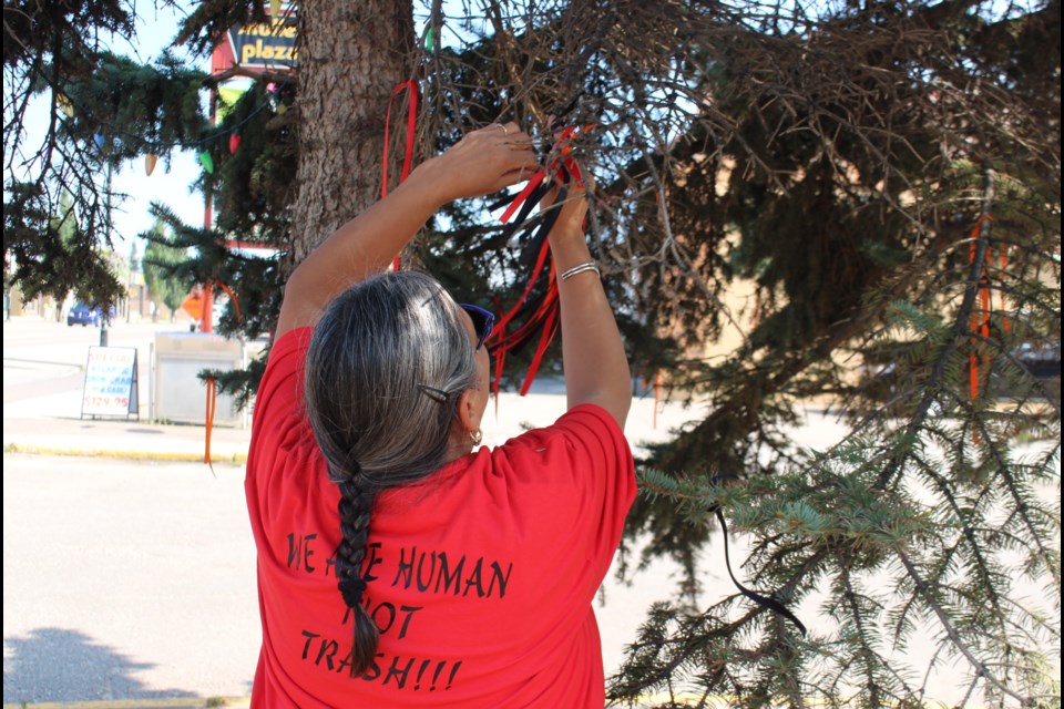 Lakeland Society for Truth and Reconciliation president Corita Vachon ties ribbons to the branches of a pine tree. The colour of each ribbon holds its own significance. Red is for the murdered and missing, orange is for the children, black is for those who are have passed on, while the purple ribbons are for the kokums (grandmothers). 