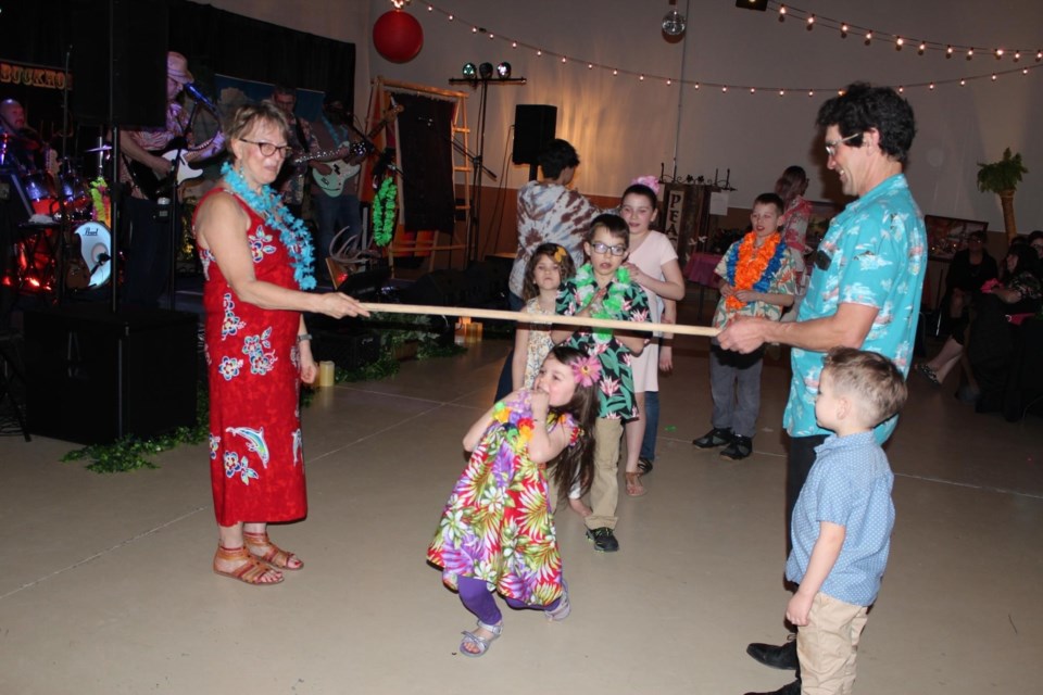 Jacki Kunec and Roger Antoniuk hold the the limbo stick as Anika Kunec limbos underneath it. / Photo courtesy of St. John's United Church