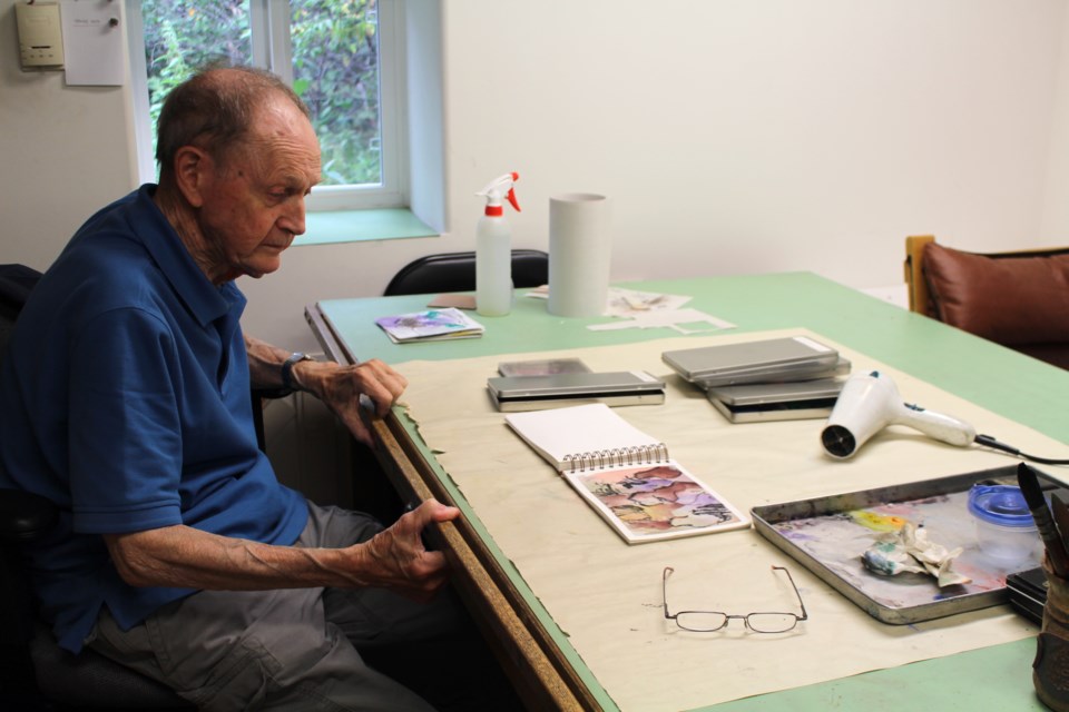 Pierre Bataillard, 78, pulls up his chair to his work bench where he paints and draws nearly every day.