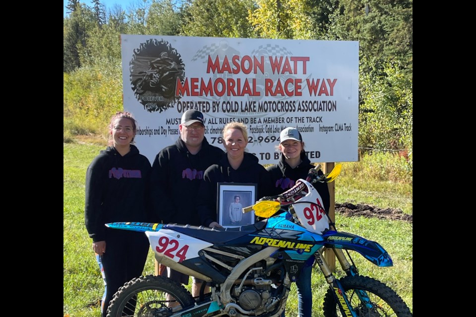 The Watt family, parents Trevor and Tara, and siblings Madi and McKenna pose with Mason's bike in front of the Mason Watt Memorial Race Way sign in Cold Lake.