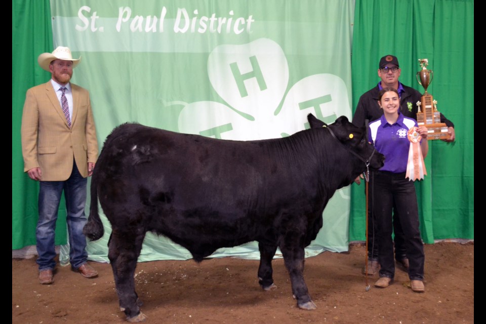 Hayden Feland of the St. Lina 4-H Beef Club accepted the Grand Champion trophy from club leader David Dechaine for her 1,288-pound steer chosen by judge Colton Hamilton (right) from a lineup of 16 finalists at the 2025 St. Paul 4-H District Steer Show, and was sold to the Canalta Hotel for $6.75 per pound.