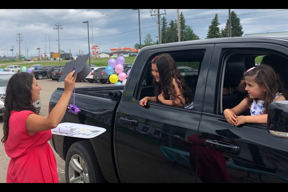 Lac La Biche's Vera M . Welsh Kindergarten teacher Charissa Delaire has a grad cap and cheers for Neda Othman who is going into Grade 1. Neda, her sister Saja — who will be entering playschool —  and her parents, were part of last Tuesday's 'wave-through' at the school.