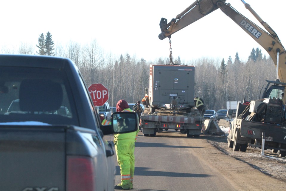 A crew member holds back westbound traffic as a large power plant is loaded onto a trailer in the construction area where a new, larger culvert is being placed to reduce flooding risks.     Image Rob McKinley
