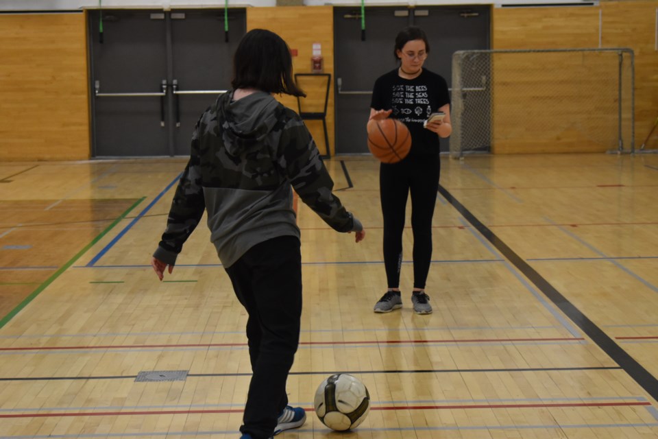 Mary on her phone dribbling a basketball, and Ella with a soccer ball