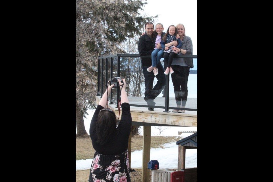 Photographer Jamie Beilstein reaches for a nice shot of the Black family on their deck during a Porch Portrait session on Friday.