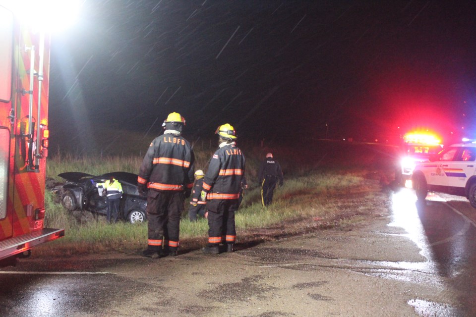 Through a steady drizzle, firefighters, ambulance personnel and RCMP investigate an early morning crash at the intersection of 91 Avenue and Highway 881. 
Image: Rob McKinley