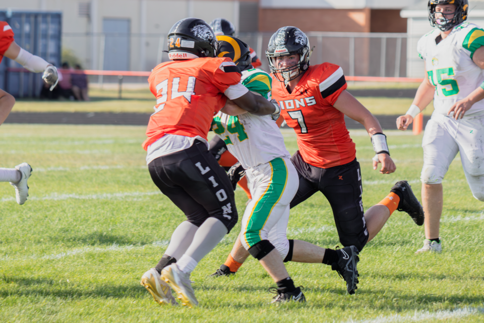 Patrick Sesay (#24) and Zack Germain of the St. Paul Lions block a Lacombe Rams carrier.