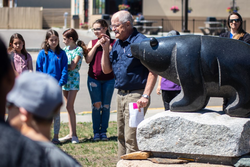 Artist Herman Poulin (blue shirt) teaches students about the Four Legged Spirit Being statue by artist Stewart Steinhauer. The statue, in addition to the "Every Child Matters" monument (not pictured) symbolizes strength, protection, healing, and a depiction of the journey toward truth and reconciliation.