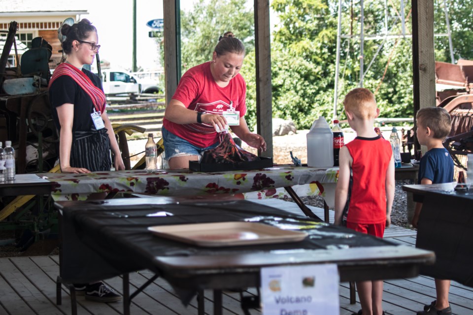 Elise Proulx (left) and Sakura Lalonde, who work at the St. Paul Museum as summer students, show a volcano demonstration to kids.