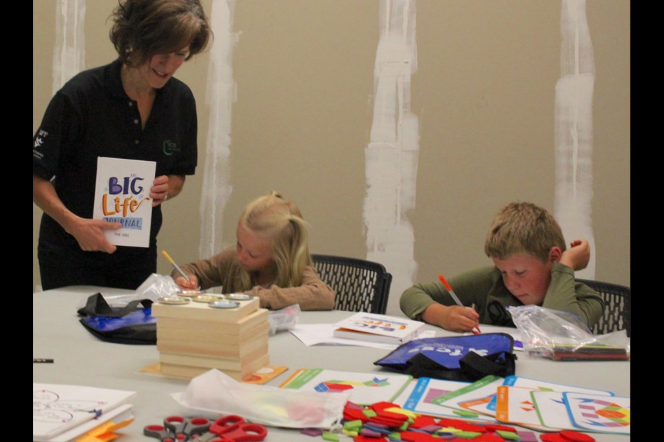 Deb Menard, FCSS community outreach worker for children, helps London Miller and Devon Campbell with a coloring project as part of the Growing Minds program at the Bold Center. 
