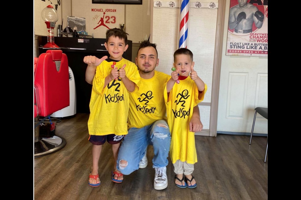 Barber Omar Saleh with two young customers in KidSport shirts. The recent barbecue lunch and haircut donation raised $1,950 for the local KidSport group.