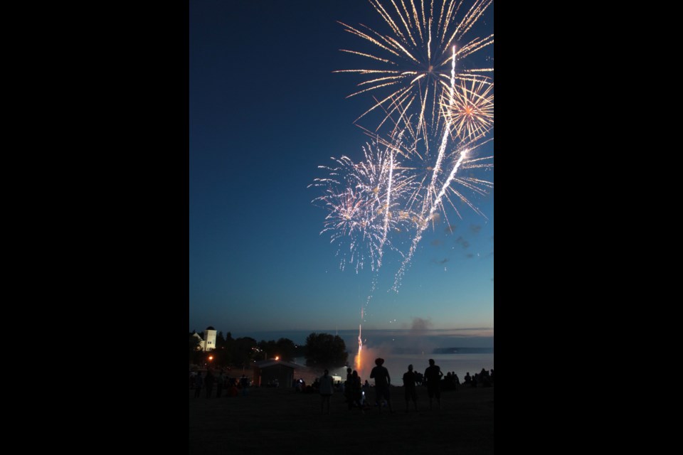 The lights of McArthur Place shine below the bright fireworks set off on Canada Day on the Lac La Biche lakeshore.      Image Rob McKinley