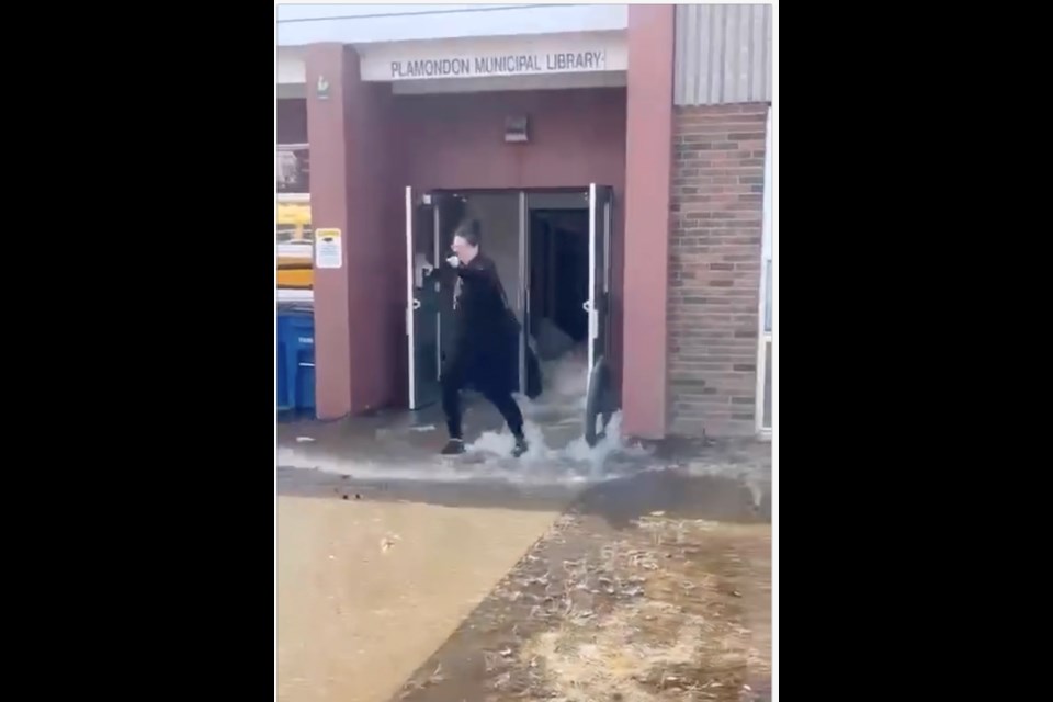 A screen-grab of video showing a person trying to avoid waves of water flowing from the community library entrance at the Ecole Plamondon School. The flood saw one empty classroom filled with water and waves of water crashing through hallways. 