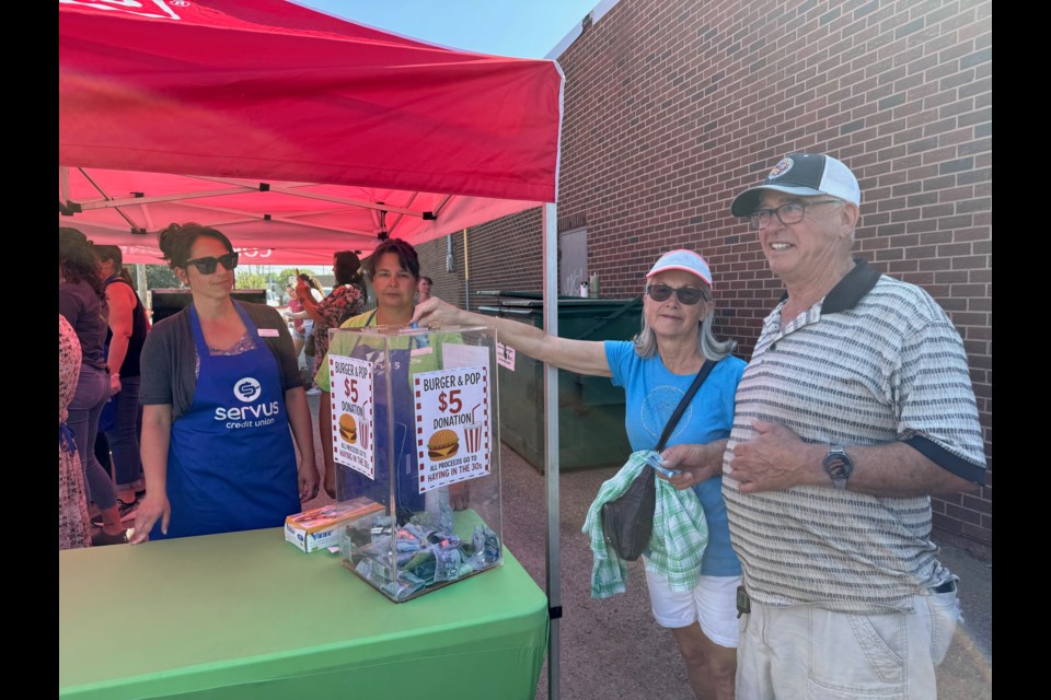 Marlene and Leo Labrie made their donations to Haying in the 30s in exchange for a burger cooked up by the staff of Servus Credit Union and Cornerstone Co-op. (Back left) Serena Kennedy and Nicole Goertzen.