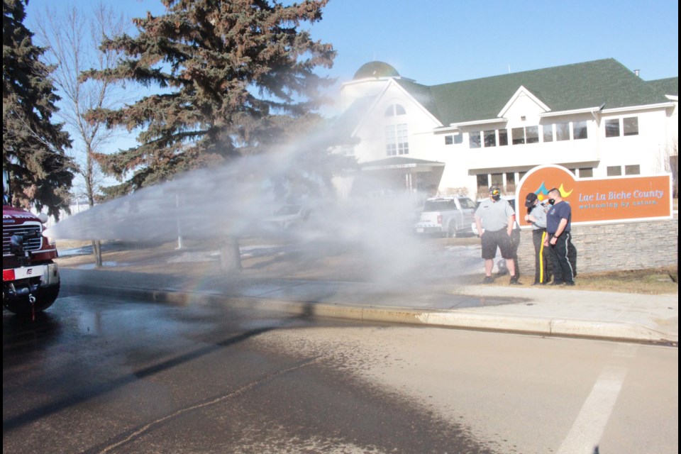 Water from the fire truck sprays towards the three Lac La Biche officers who volunteered to get soaked if Portage College Social Work students raised $1,000 for the local homeless shelter.    Image Rob McKinley.