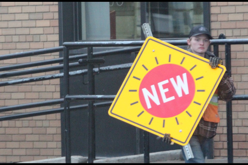 A Lac La Biche County staffer carries a new sign marker to install near the intersection of 102 Ave and 101  Street near Lac La Biche's Canada POST and the Abougouche AG Foods grocery store.