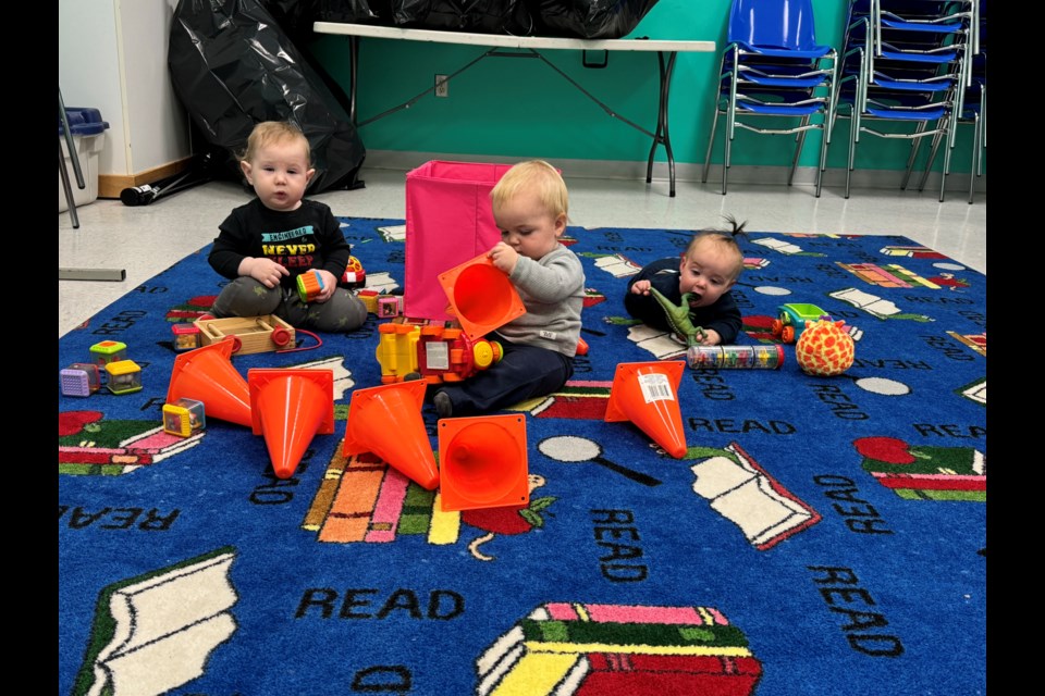 Younger siblings hang out and play with age appropriate toys while older kids and parents participate in a library program.