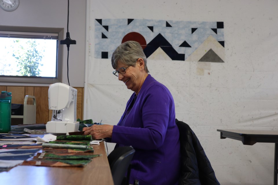 Trudy Champagne with the Quilting Bees Guild and one of her crafter quilts on the background.