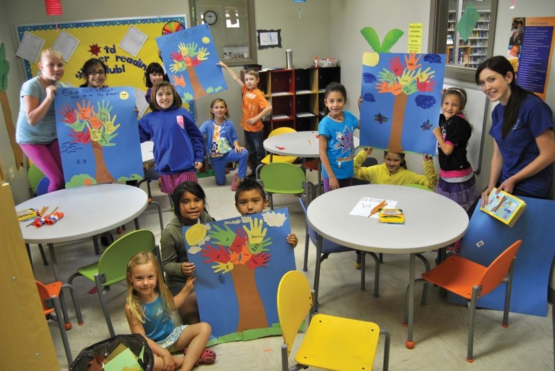 Several children participating in the Bonnyville library&#8217;s 2013 Summer Reading Program pose with their &#8216;Save our Trees&#8217; craft they made, alongside guest