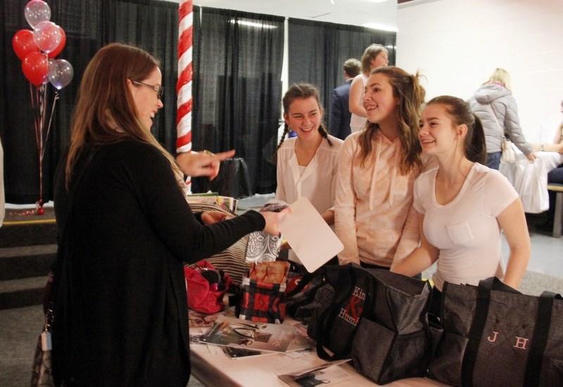 Elizabeth-Ann Switzer stops at a table to discuss the product Grade 9 students (left to right) Allyson Carr, Emma Tercier, and Patience Colbourne are selling.