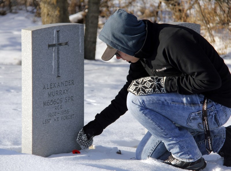 Jarred Dargis places a poppy in the snow next to the headstone of a deceased soldier during the No Stone Left Alone project.