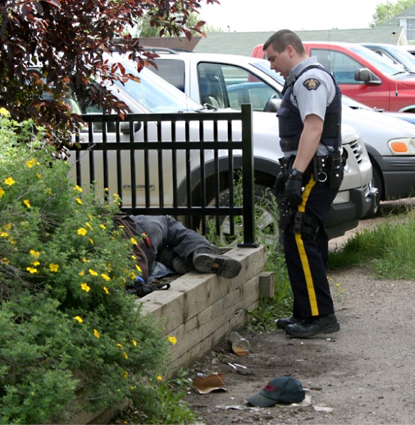 A man lays in the garden in the park on 50th Avenue on Friday afternoon with an open liquor bottle at his feet. An RCMP officer attended the scene and escorted the man in