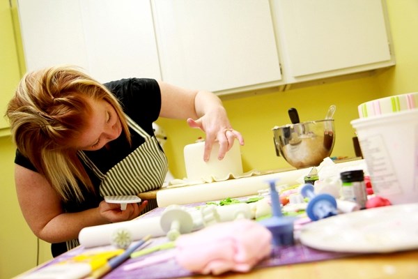 Lori Hynes, owner and creator at Lori&#8217;s Sweet Cakes, pays close attention to detail as she attaches strips of fondant onto a cake.