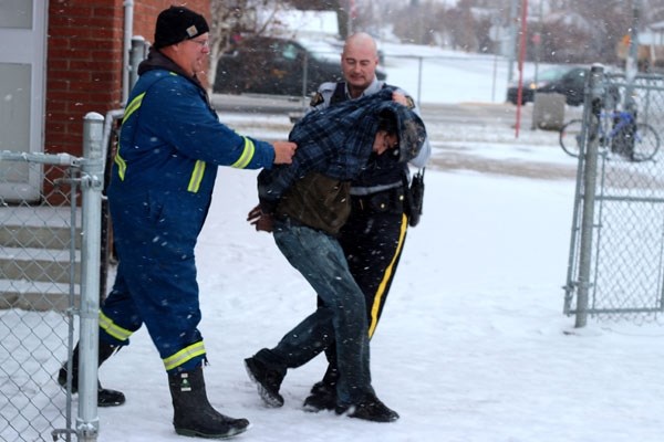 An RCMP member leads a suspect away from the scene of the Racette School crash on Oct. 25 morning. Richard Benson, a 46-year-old St. Paul man, is facing charges of criminal