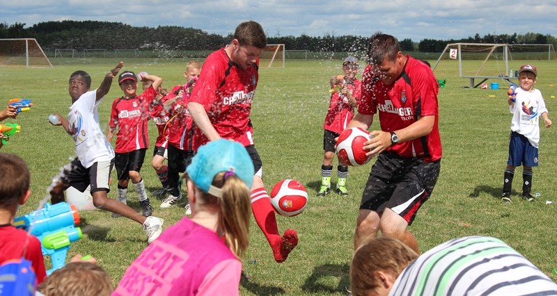 Coaches Chris Duff and Mark Austin try to juggle soccer balls while kids from the British Soccer Camp soak them with water balloons and water guns last Friday.