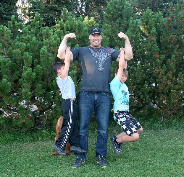 Elijah Hall, two-time champion of the Elk Point and Cold Lake Strong Man Competitions, poses while lifting his sons, Austin and Daniel, on each arm.
