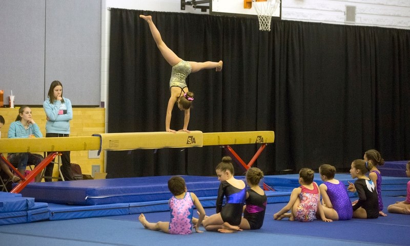 Maya Yakiwchuk performs on the beam while other young competitors watch from the floor.