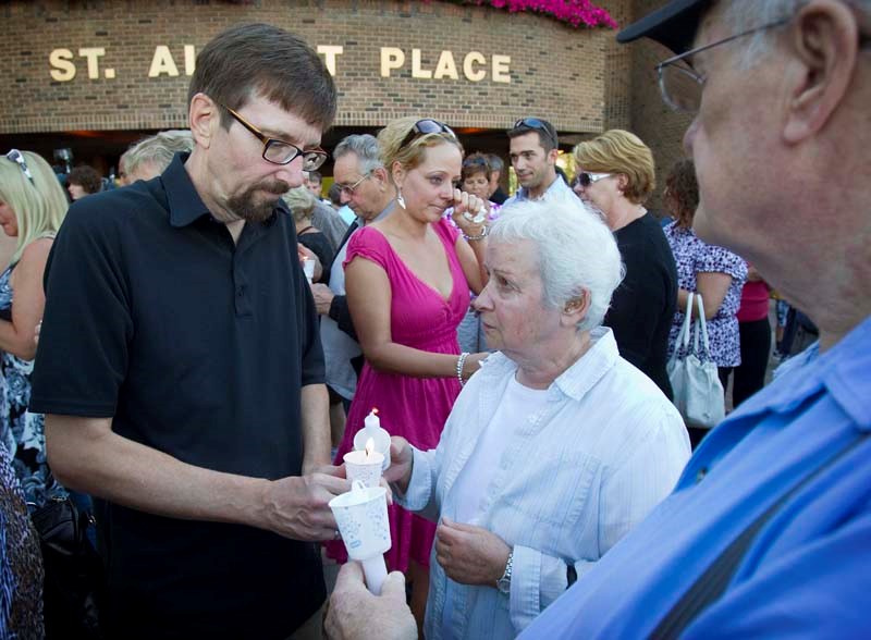 Bret McCann pass on the flame during a candlelight vigil of hope for his missing parents, Lyle and Marie McCann, outside St. Albert Place Saturday evening.