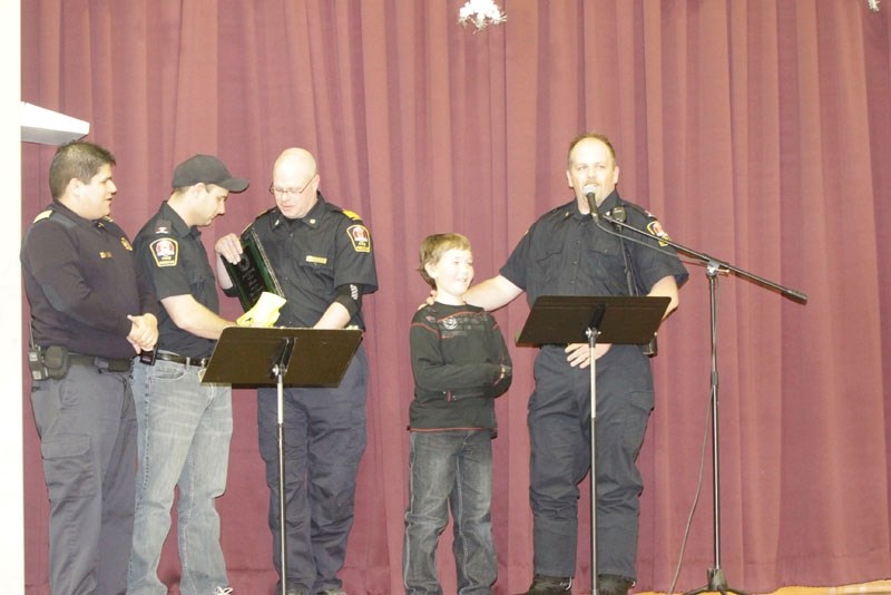 Elijah Skoglund, 8, receives a hero award from members of the area&#8217;s fire departments for rescuing his brother from a rain barrel last summer