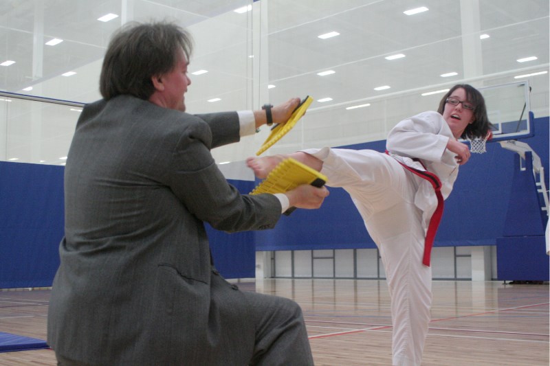 Taekwondo student Sarah Lewiski kicks through the board while coach Glenn Doubt held the board at last Wednesday&#8217;s taekwondo belt testing at the Bold Center.