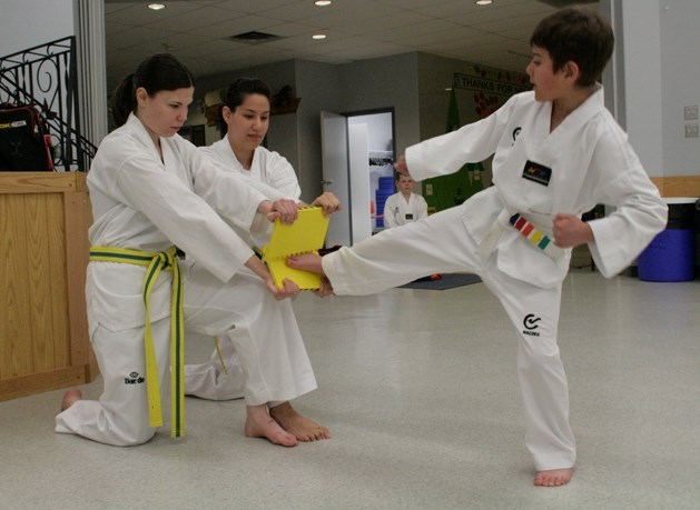 Adam Abougouche, 9, kicks a board that Lauren Mischuk and Heidi Hartmann hold up. The taekwondo club is working on raising money for the Hope Haven Women&#8217;s Shelter.