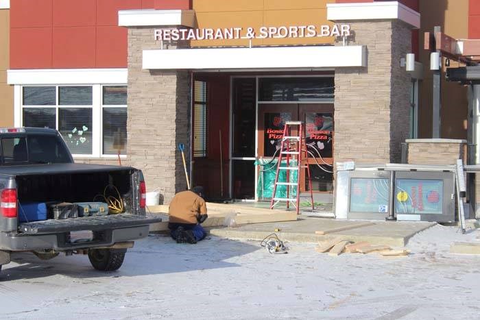A man repairs damage to the Boston Pizza in Lac La Biche Feb 7 after a stolen vehicle was used to steal an ATM. Police believe the same group of suspects may be behind 10