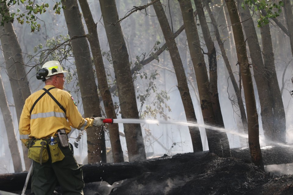 A firefighter sprays the wildfire on land near Plamondon.