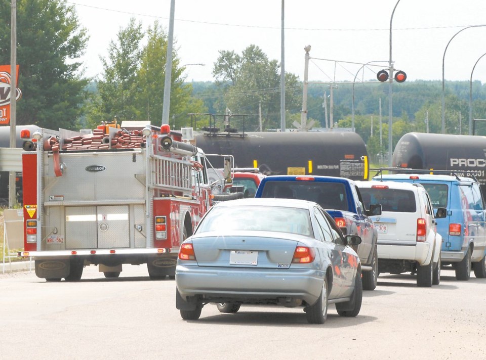 Vehicles, including a fire truck, line up along 103 Street, waiting for a train to pass.