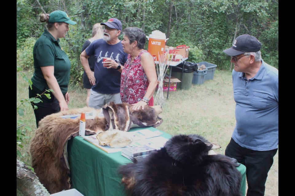 Jaclyn Denman, a visitor engagement specialist with Alberta Parks, talks with Martin Straus and Maria Straus while Bill Sallee checks out the bear hides that were on display at Sir Winston Churchill Provincial Park for the July 8 Coffee and Connections event. Chris McGarry photo. 
