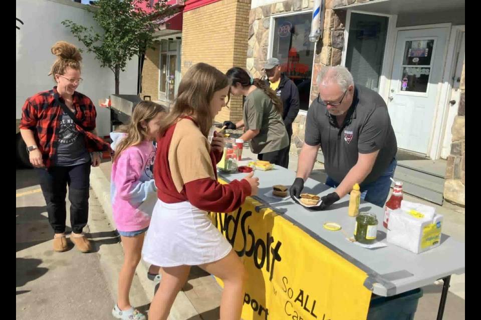 Jim Knight, a member KidSport Lac La Biche, serves up burgers to Asia and Hadley Flumian during the barbeque held on Aug. 15 to raise money for the organization. Chris McGarry photo. 