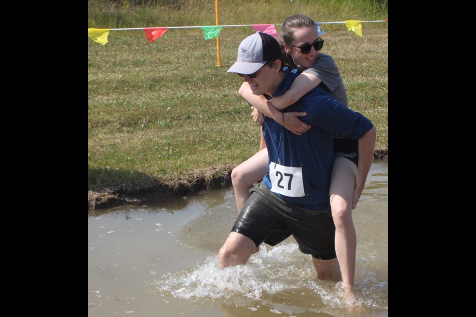Jonathan and Nica Schultz, the first-place winners in the 2025 Alberta Wife Carrying Championship, make their way through the water pit on the racecourse at the Lakeland Agricom in Lac La Biche during the event, which took place on Aug. 1. Chris McGarry photo.