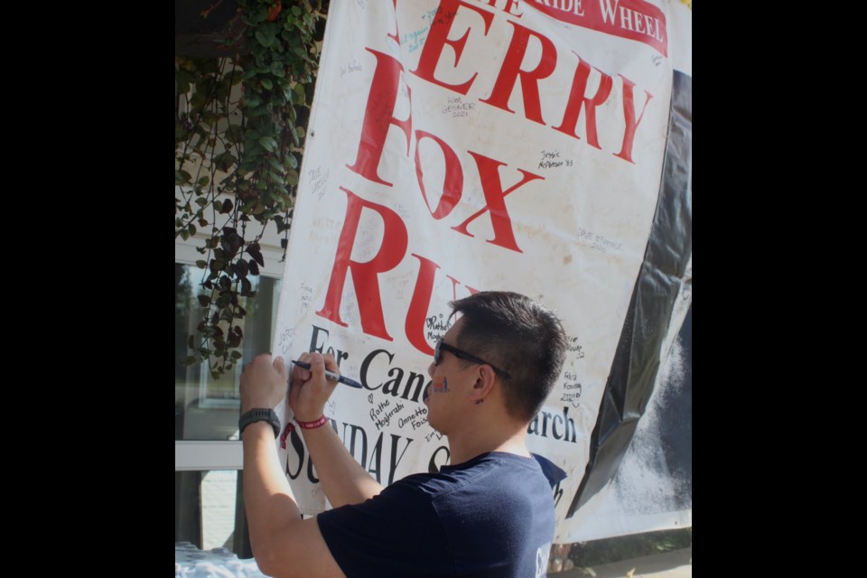 Jordan Chan, whose father, Gene Chan, died of cancer in 2018, signs his name on the Terry Fox banner hanging over the entrance to McArthur Place. Chris McGarry photo. 
