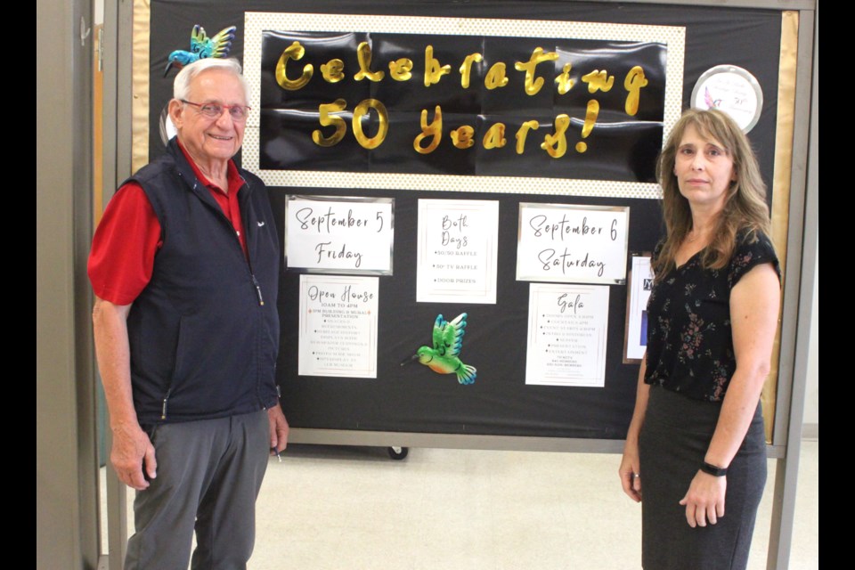 Les Diachinsky, president of the Lac La Biche Heritage Society, and Stacey St. Jean, executive director, stand in front of a sign inside the building marking the 50th anniversary of the organization and events that will be taking place on Sept. 5 and 6. Chris McGarry photo. 