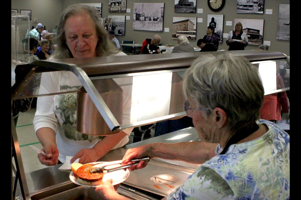 Davina Vetzal serves up a hamburger to Mona Frederick during the barbecue and bake auction which were held at the Lac La Biche Heritage Centre on Saturday, June 8. 