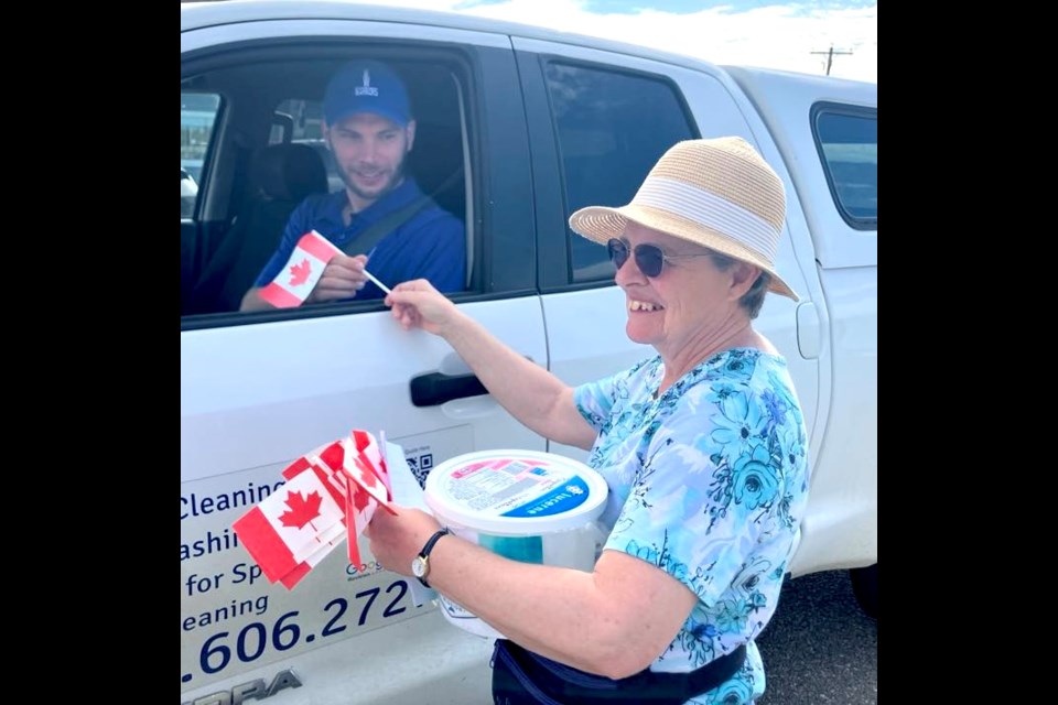 Priscilla Cloutier was all smiles as she handed out Canadian flags and programs for the Canada Day event that took place at the Lac La Biche Mission on July 1. Cloutier gives one of these flags to David Schultz, who stopped by the Mission bright and early to take in the festivities. Chris McGarry photo. 