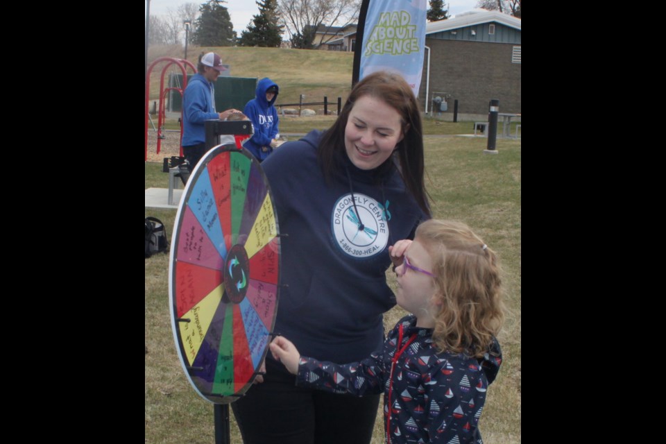 Jamie Beilstein of the Dragonfly Centre helps Lilyanna Stisson-Thompson to spin the wheel at a game that was set up in McArthur Park. Chris McGarry photo. 